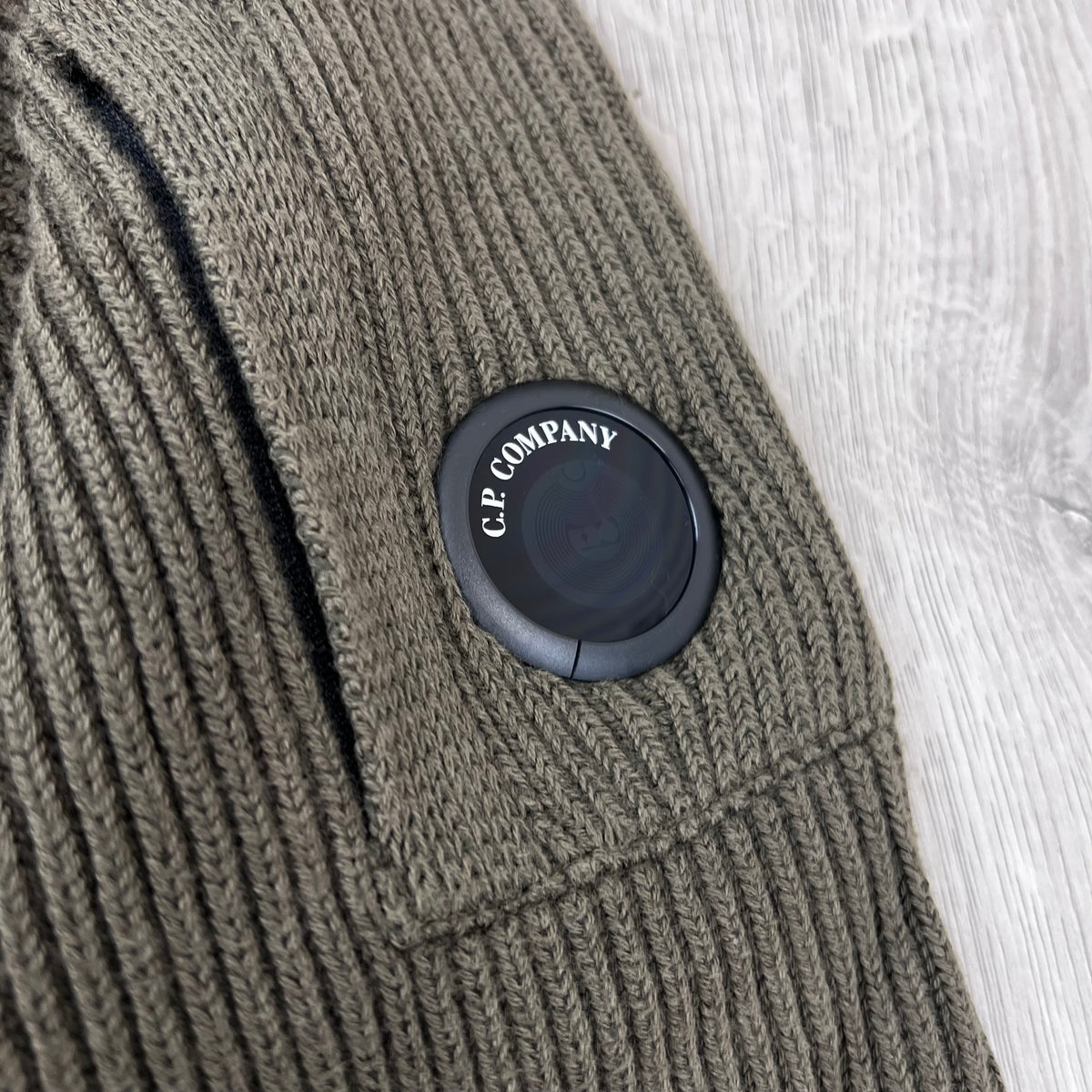 Close up view of the new NFC lens detail on a CP Company Full Rib Cotton Knit Sweatshirt in Ivy Green.