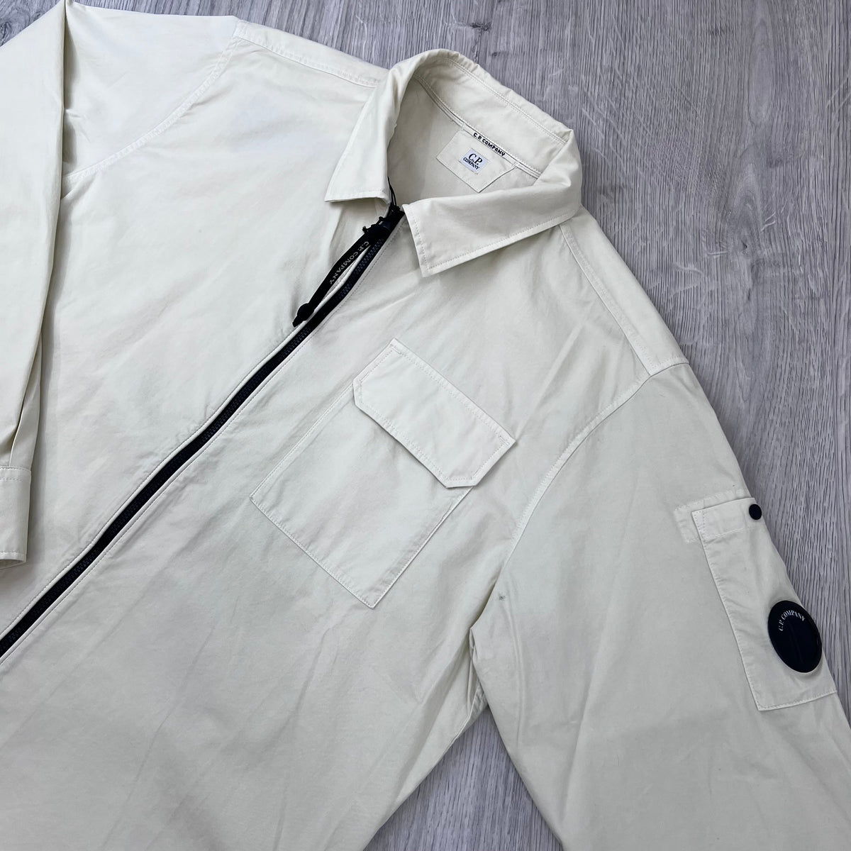 Angled view of the flap collar, sleeve lens detail and zip-closure on the CP Company Zip Overshirt in Silver Birch.