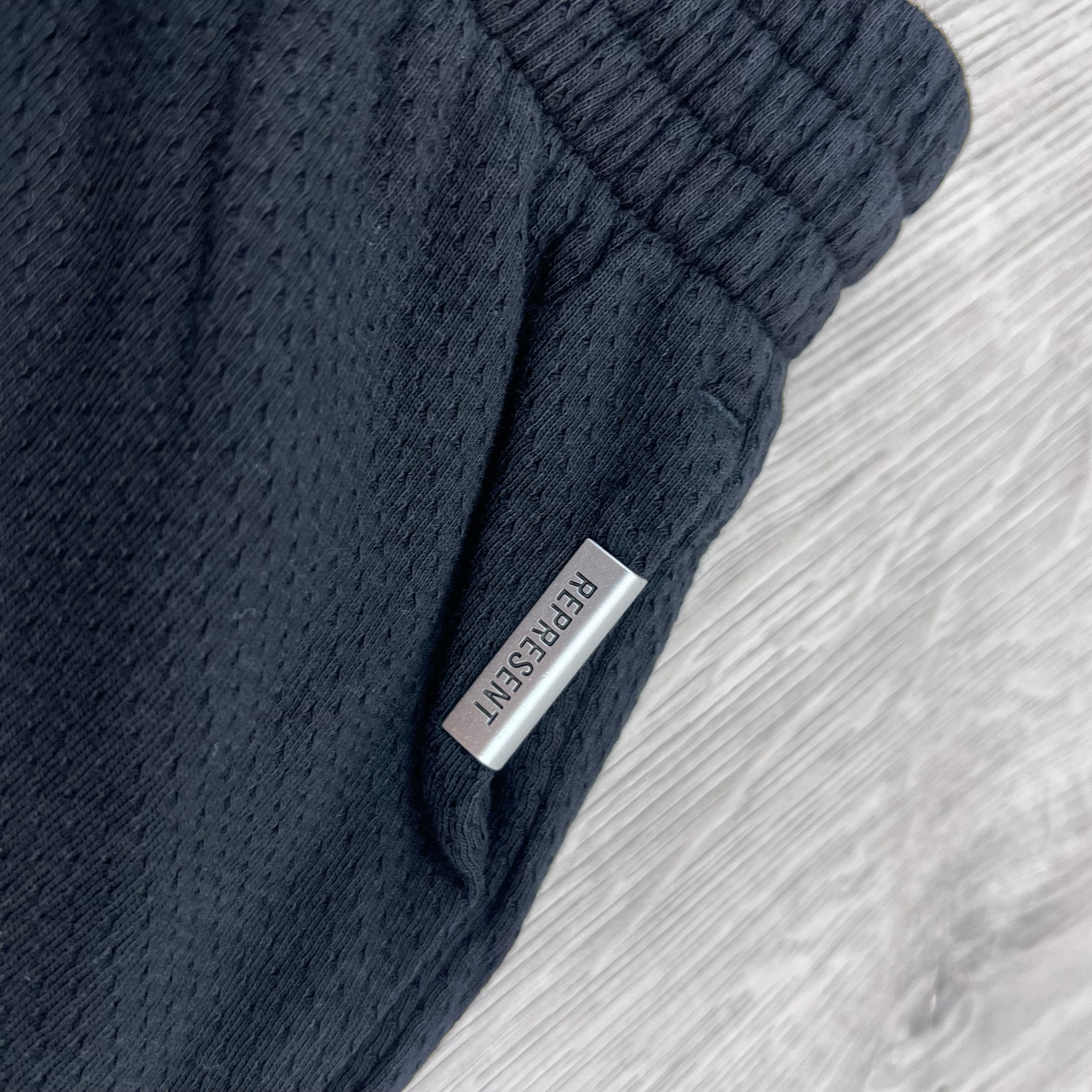 A close up view of the metal hardware detail on the Represent Owners Club Mesh Shorts in Black.