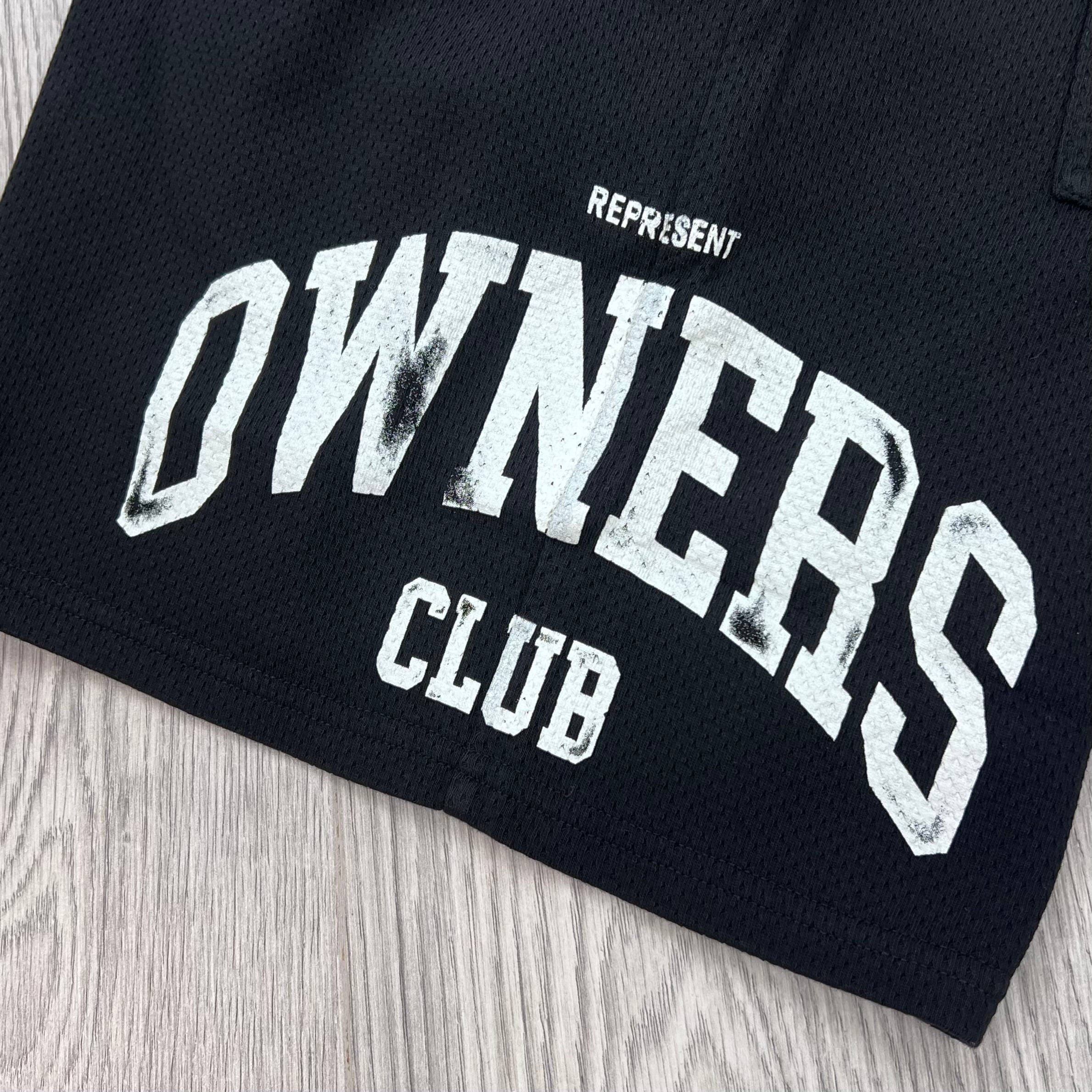 A close up view of the screen printed logo on the Represent Owners Club Mesh Shorts in Black.