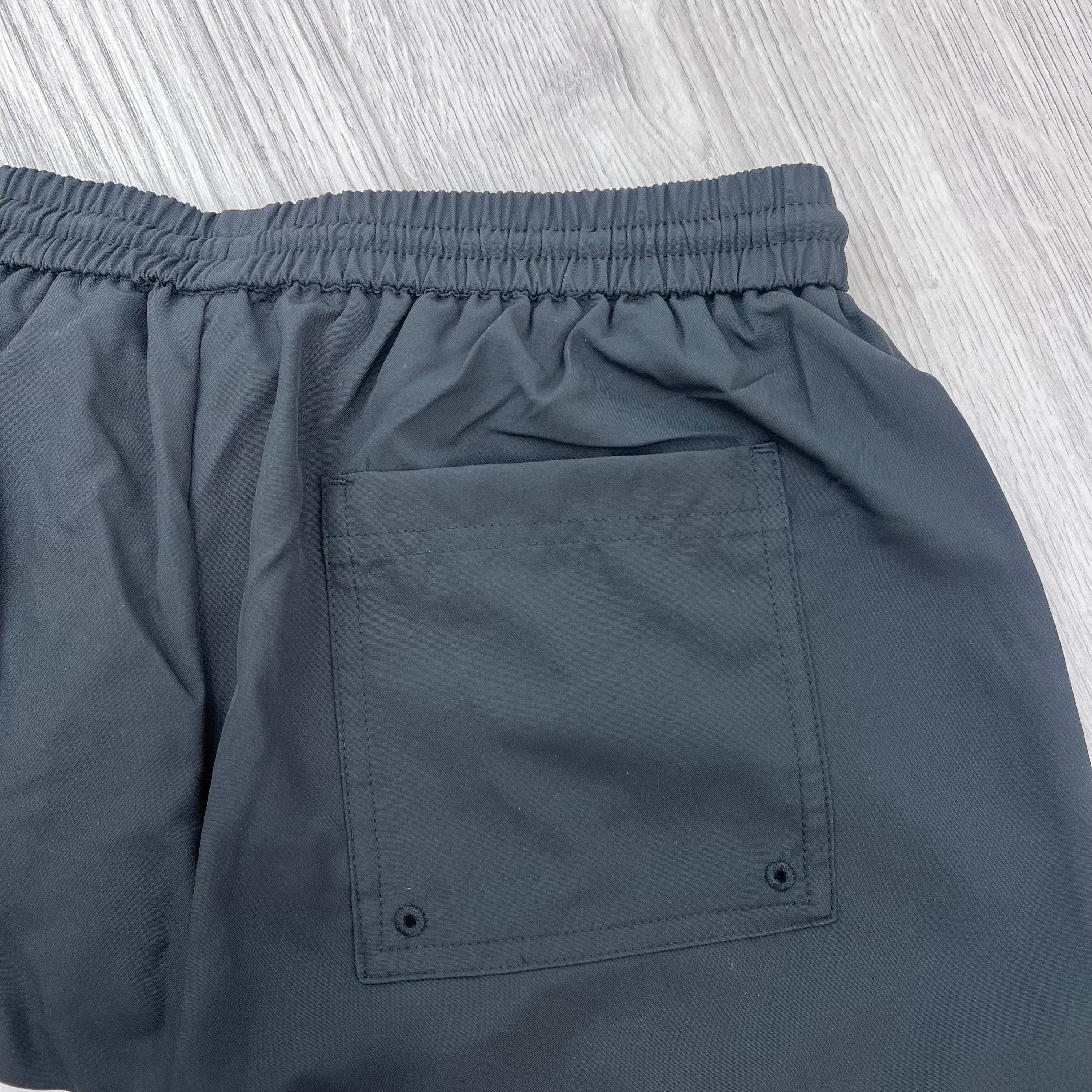 A close up view of the back pocket and waistband on the Represent Swim Shorts in Black.