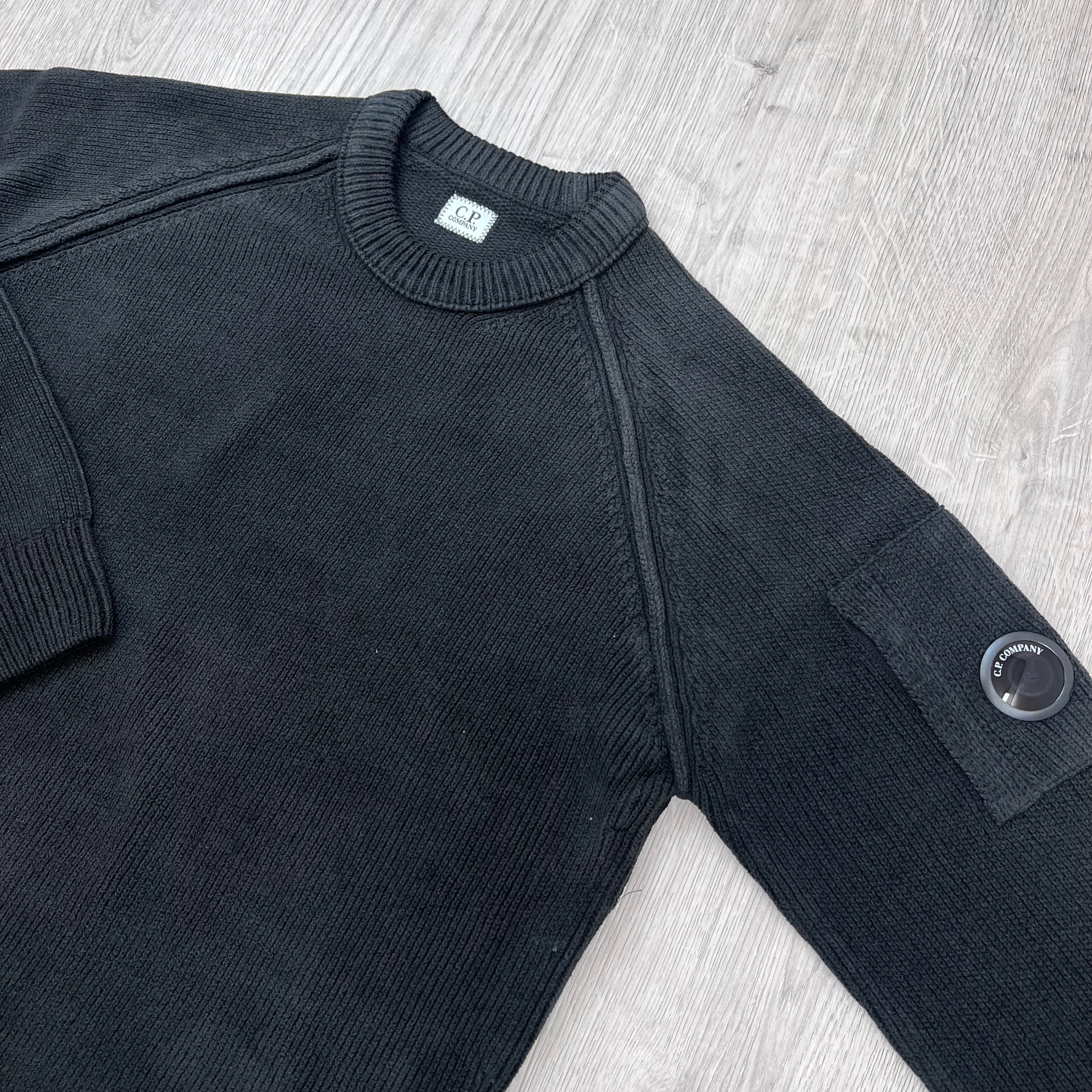 An angled view of a CP Company Chenille Cotton Lens Sweatshirt in Black showing the lens on the sleeve. 