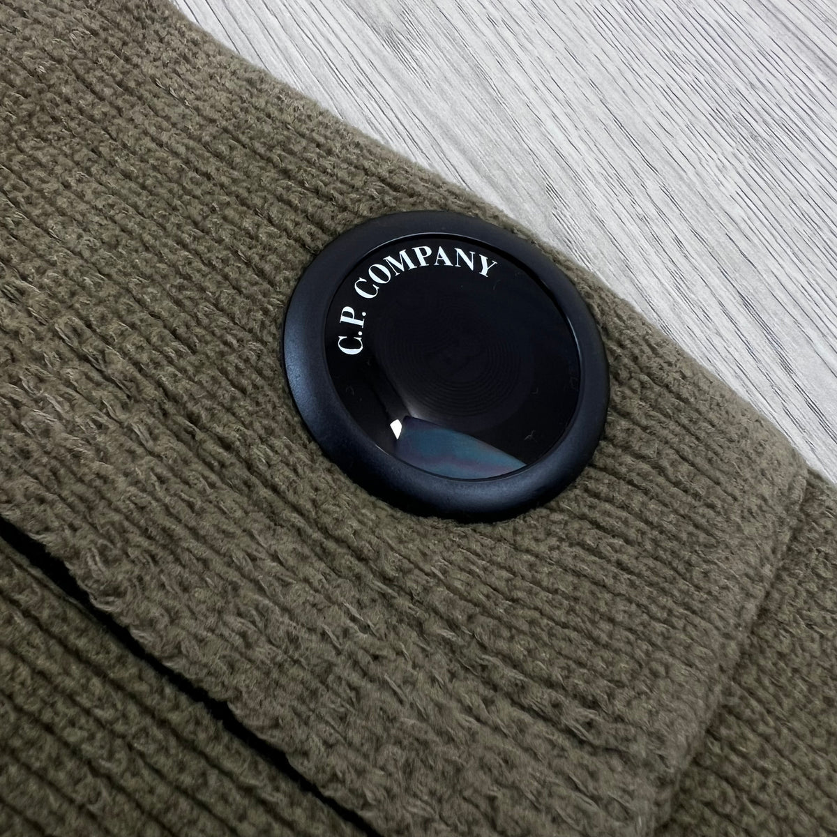 Close up view of the NFC lens detail logo on a CP Company Chenille Knit Polo Sweatshirt in Ermine.