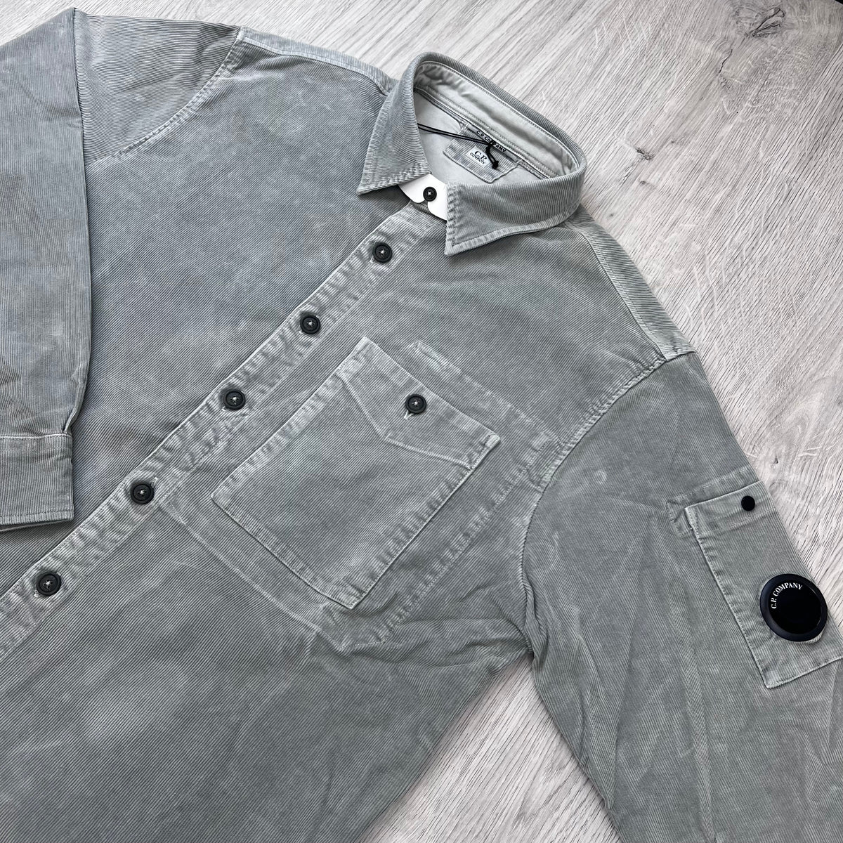 Angled view of the folded collar, button placket and sleeve lens on a CP Company Cotton Corduroy Overshirt in Flint Grey.