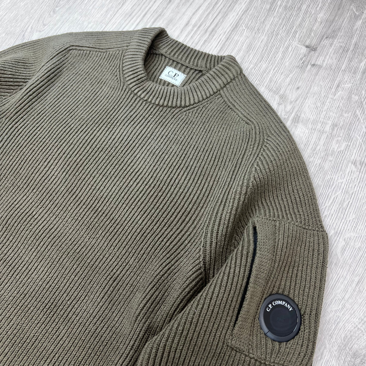 Angled view of the ribbed crewneck collar and sleeve lens on a CP Company Full Rib Cotton Knit Sweatshirt in Ivy Green.