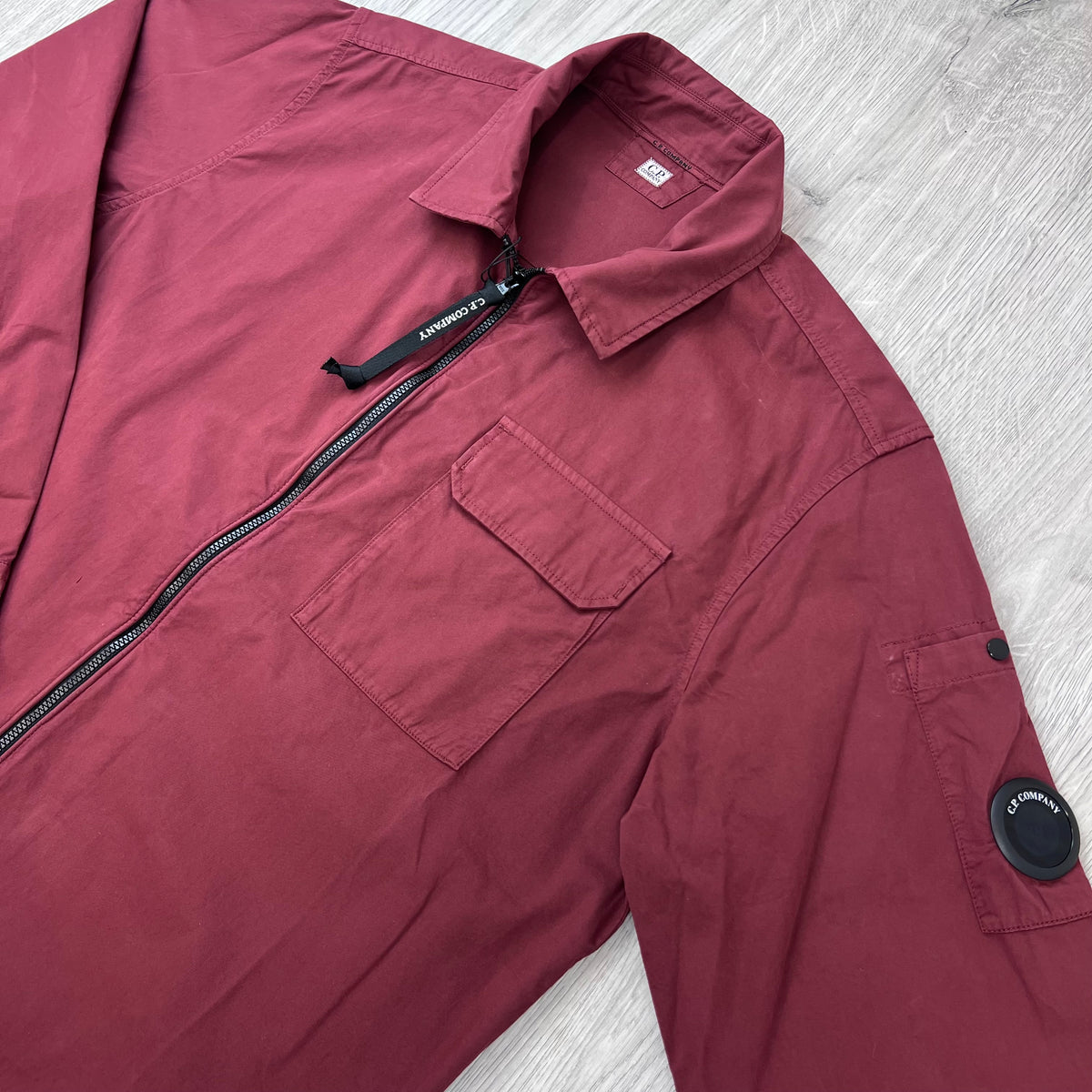 Angled view of the folded collar, zip closure and sleeve lens on a CP Company Zip Overshirt in Andorra Red. 