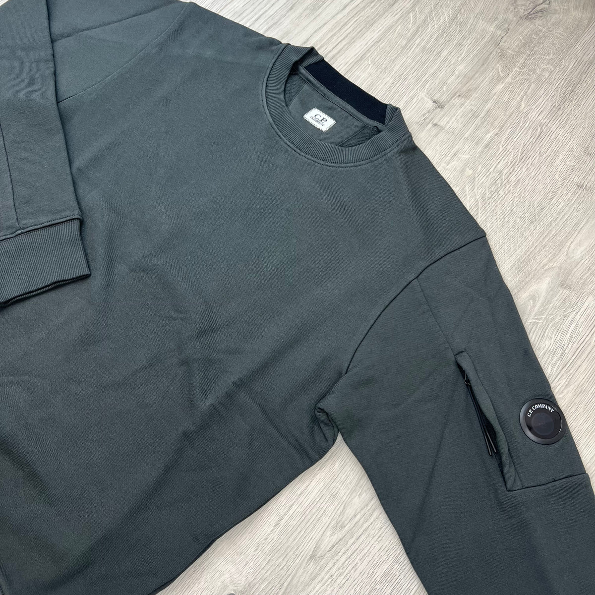 Angled view of the crewneck collar and sleeve lens detail on a CP Company Raised Fleece Sweatshirt in Raven Grey.