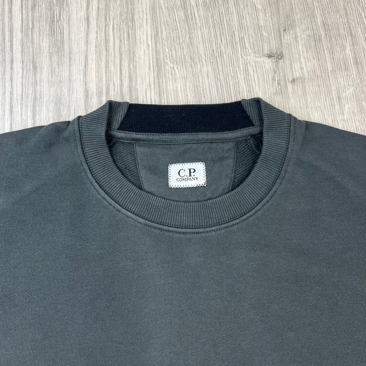 Close up view of a ribbed crewneck collar on a CP Company Raised Fleece Sweatshirt in Raven Grey. 