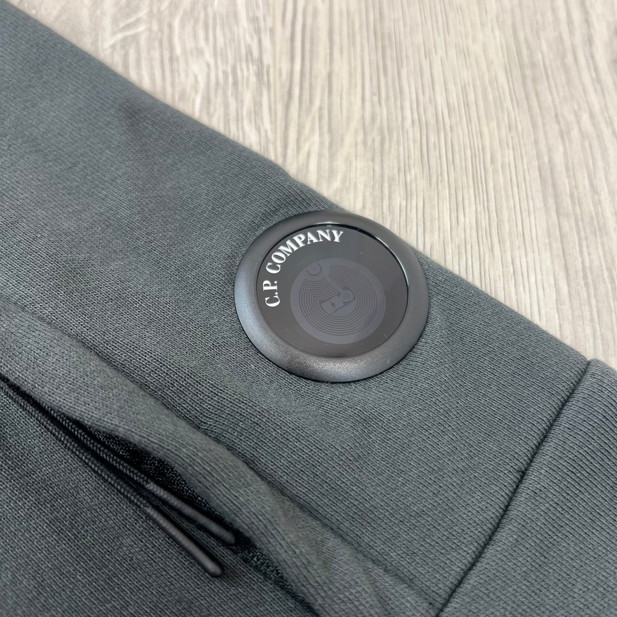 Close up view of the NFC lens detail on a CP Company Raised Fleece Sweatshirt in Raven Grey. 