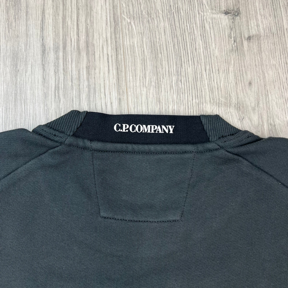 Close up view of the elasticated collar logo on a CP Company Raised Fleece Sweatshirt in Raven Grey. 