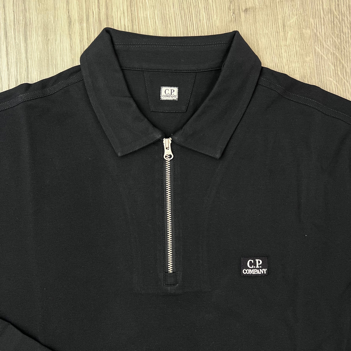 Close up view of the zip-closure placket on a CP Company Stretch Piquet Long Sleeve Polo Shirt in Navy Blue. 
