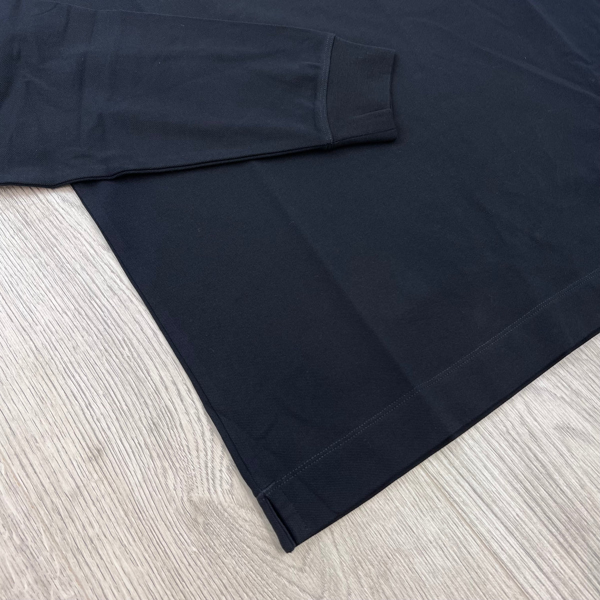 Close up view of the stitched hem and ribbed cuffs on a CP Company Stretch Piquet Long Sleeve Polo Shirt in Navy Blue. 