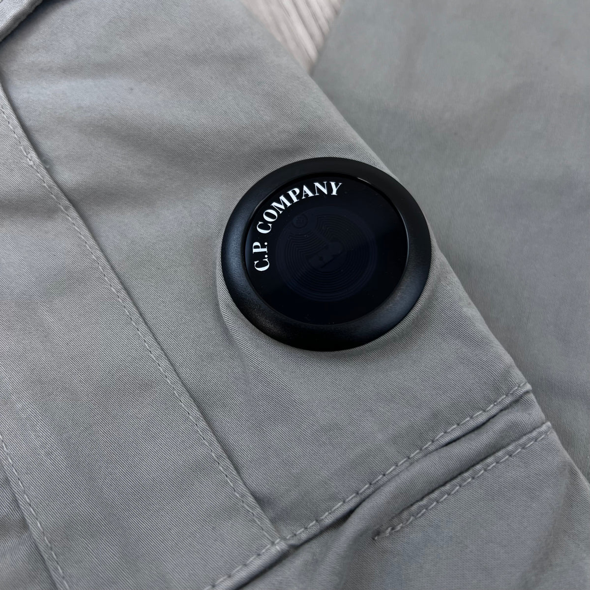 Close up view of a NFC lens detail on the CP Company Stretch Sateen Cargo Trousers in Flint Grey.
