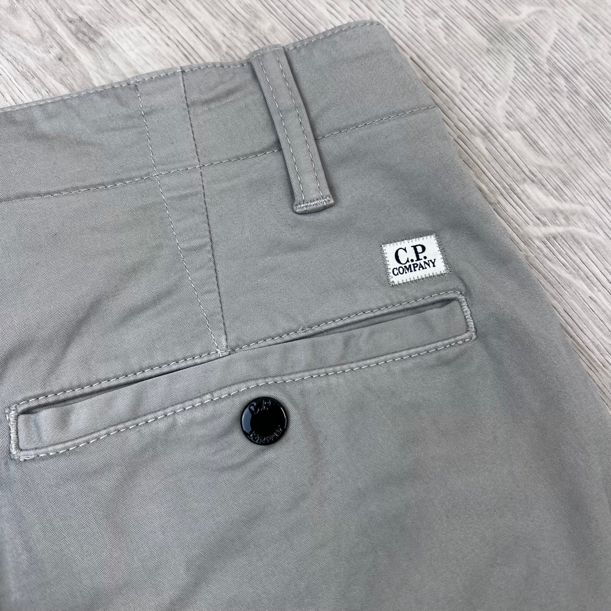 Close up view of the small patch logo on the welt pocket on the back of the CP Company Stretch Sateen Cargo Trousers in Flint Grey.