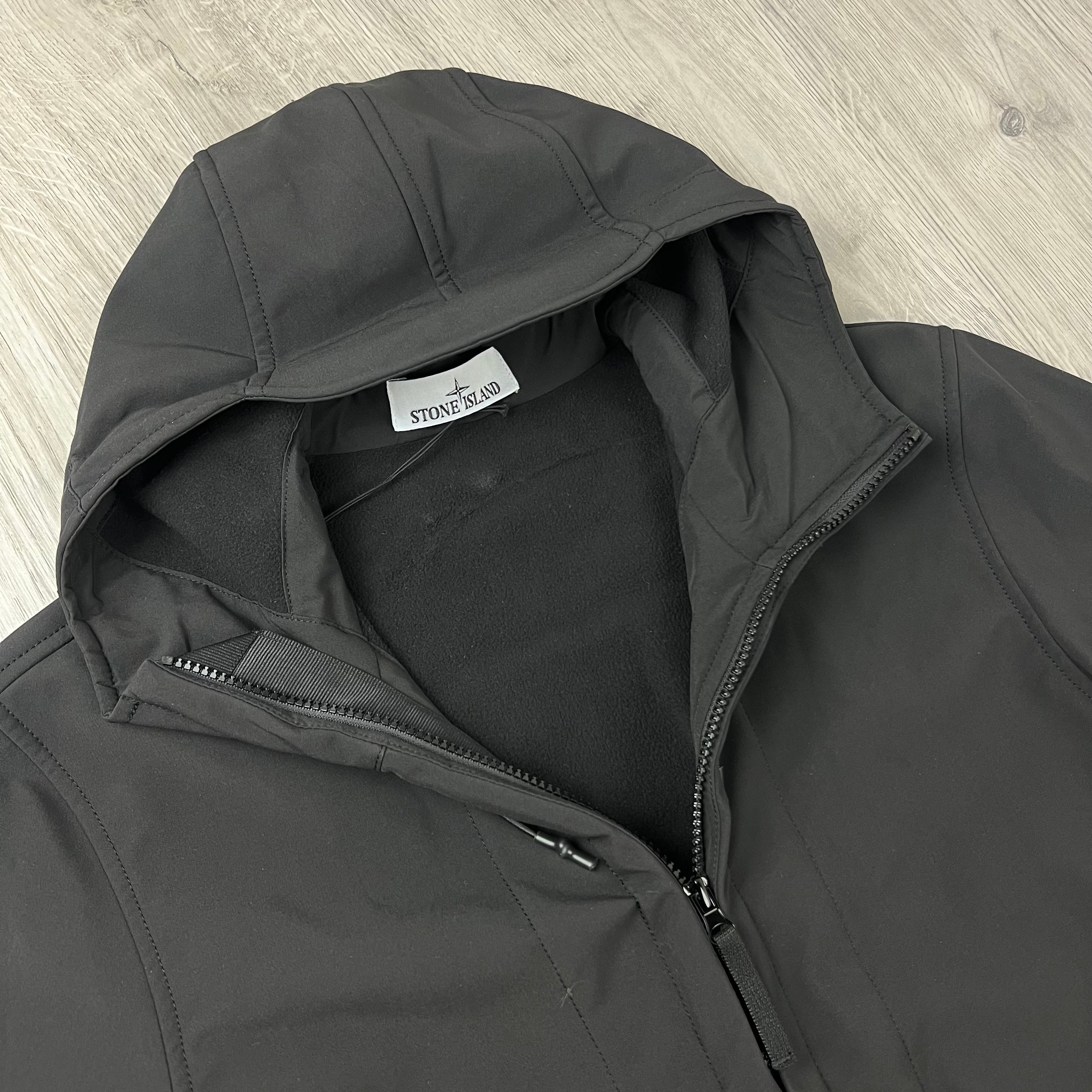 A close-up of a Stone Island Soft Shell-Re.dye Jacket in Black with a black fleece lining, featuring a visible Stone Island brand tag inside the collar.